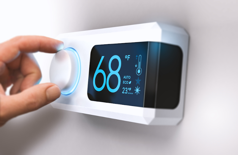 Hand turning a home thermostat knob to set temperature on energy saving mode.